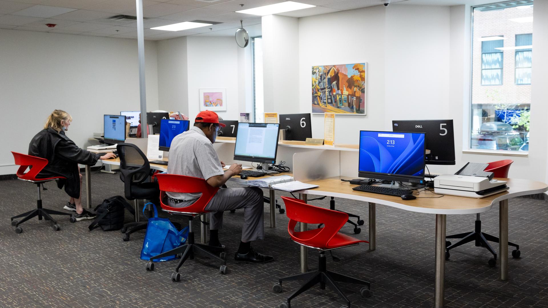 Open office space with people working at computers, red chairs, and bright lighting.