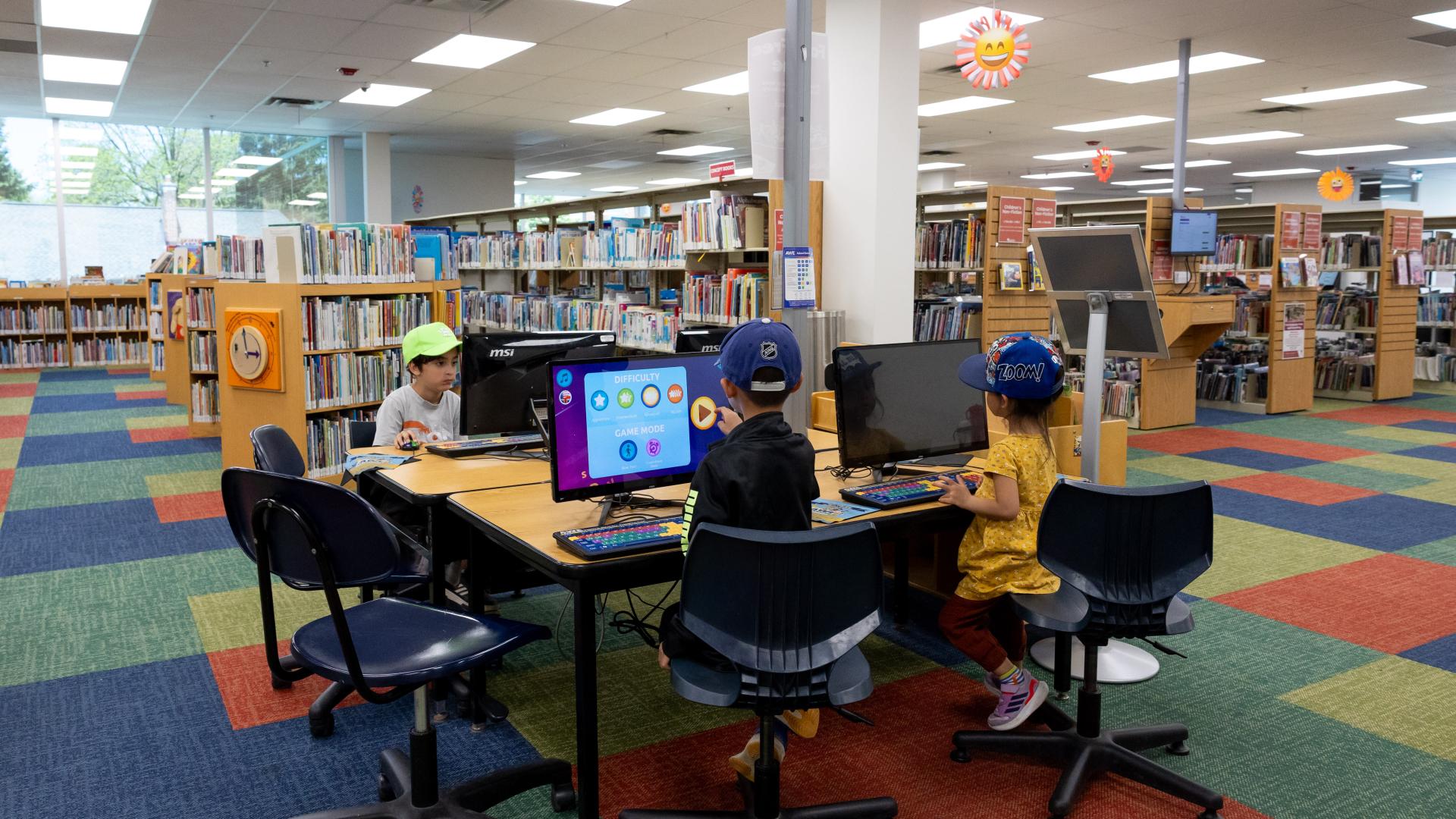 Children using computers in a colorful library setting.