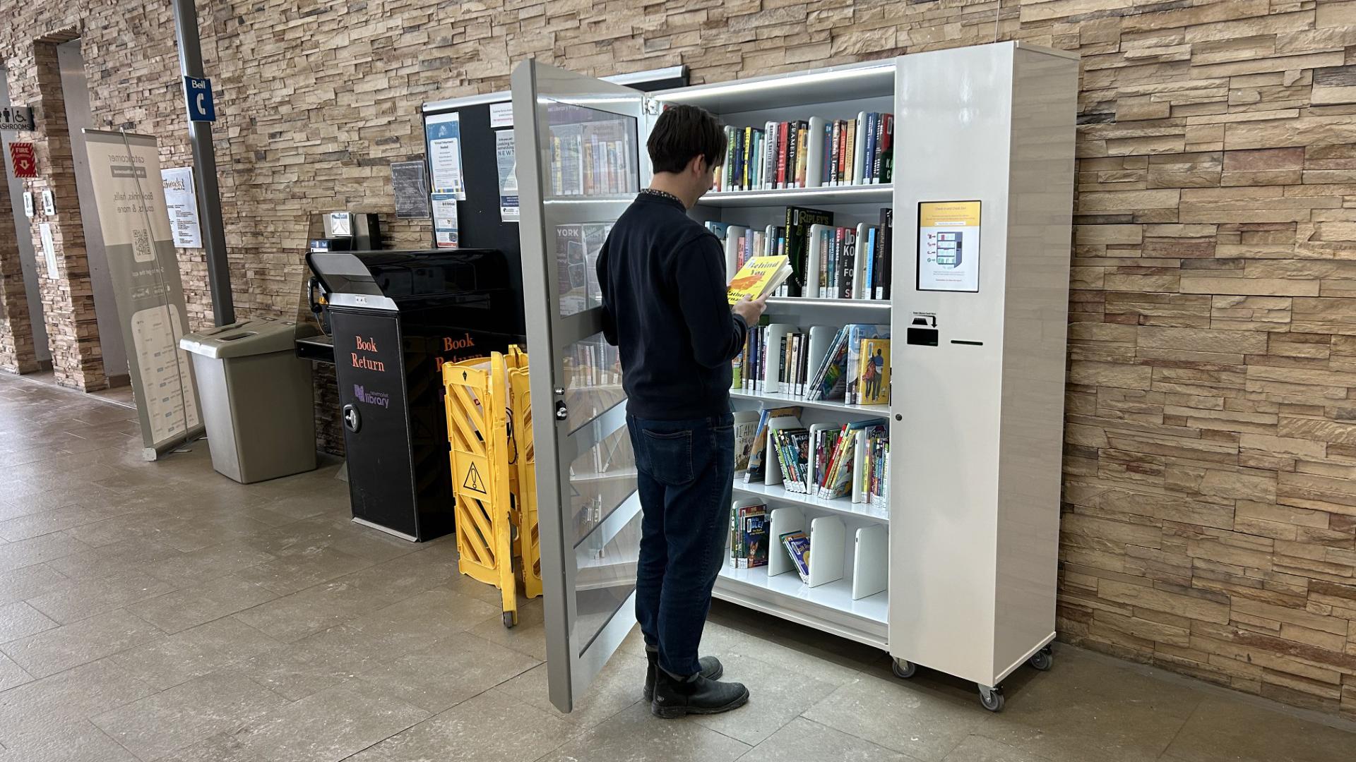 Man browsing books in a library vending machine.