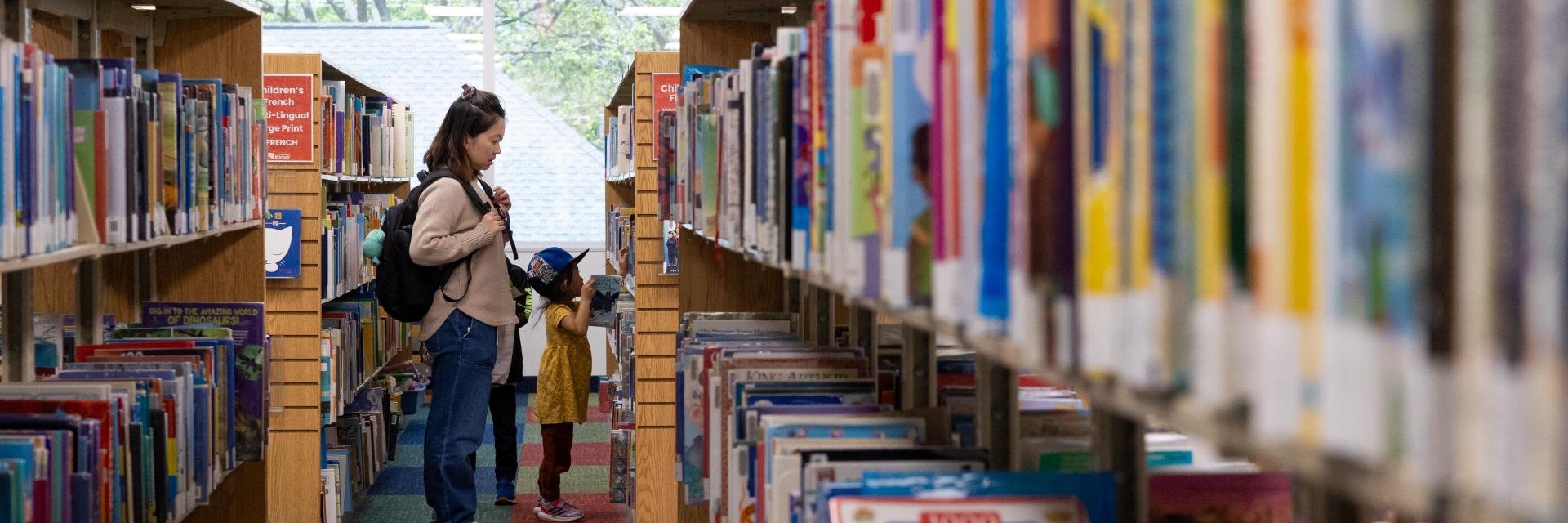 Library aisle with bookshelves, adult and child browsing books.